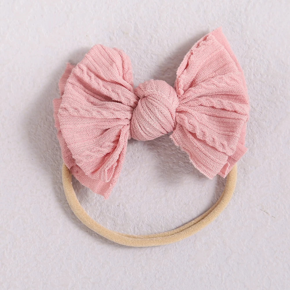 A pink fabric bow headband with a light yellow elastic band, suitable for a baby or girl.