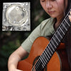 A close-up of silver-plated nylon classical guitar strings being strung on a wooden acoustic guitar.