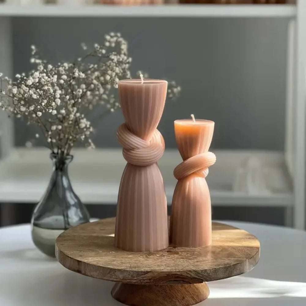 A pink ribbed silicone candle mold is displayed on a wooden stand with a bundle of dried flowers in the background.