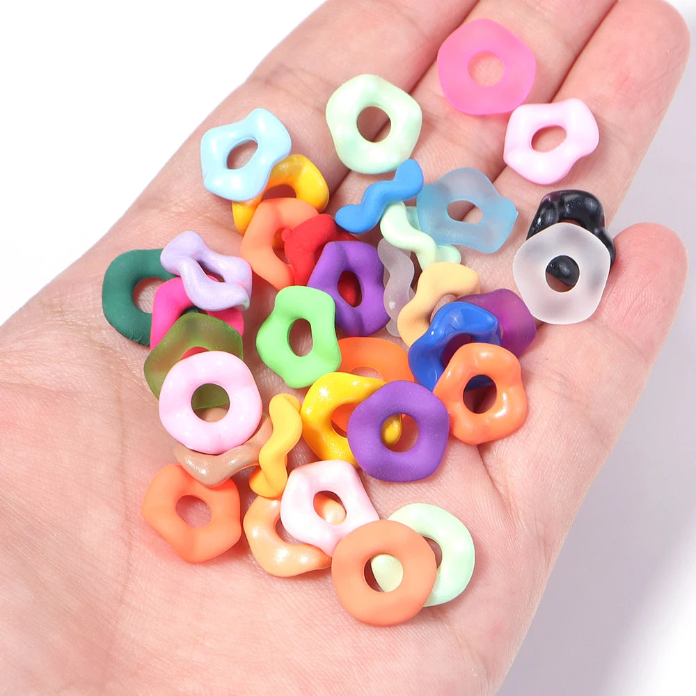 A hand holds an assortment of colorful acrylic spacer beads in various shapes and sizes.