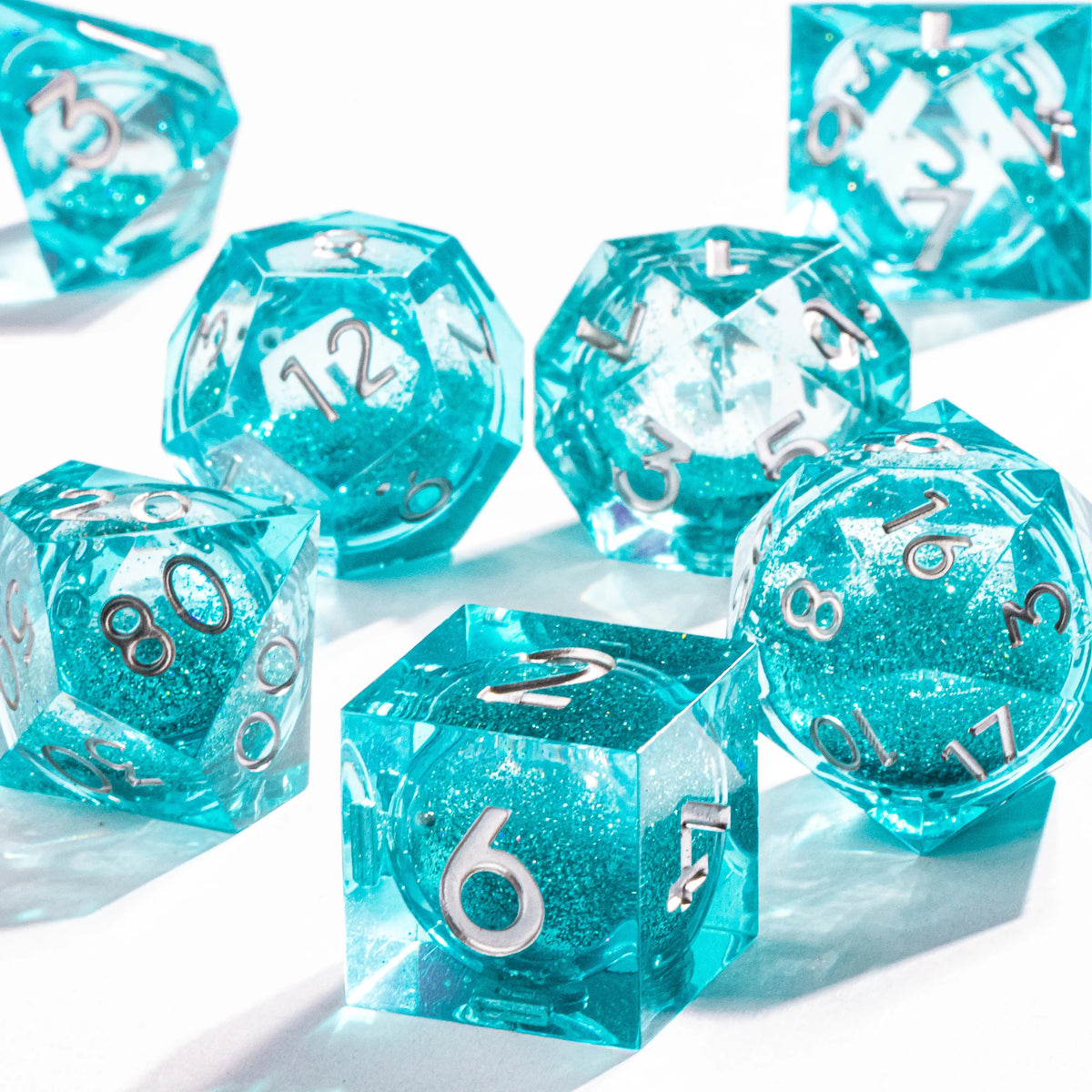 A collection of translucent blue liquid core polyhedral dice with a galaxy finish scattered on a white surface.