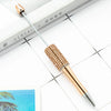 A gold-colored beaded ballpoint pen is shown resting on a white surface next to a book.