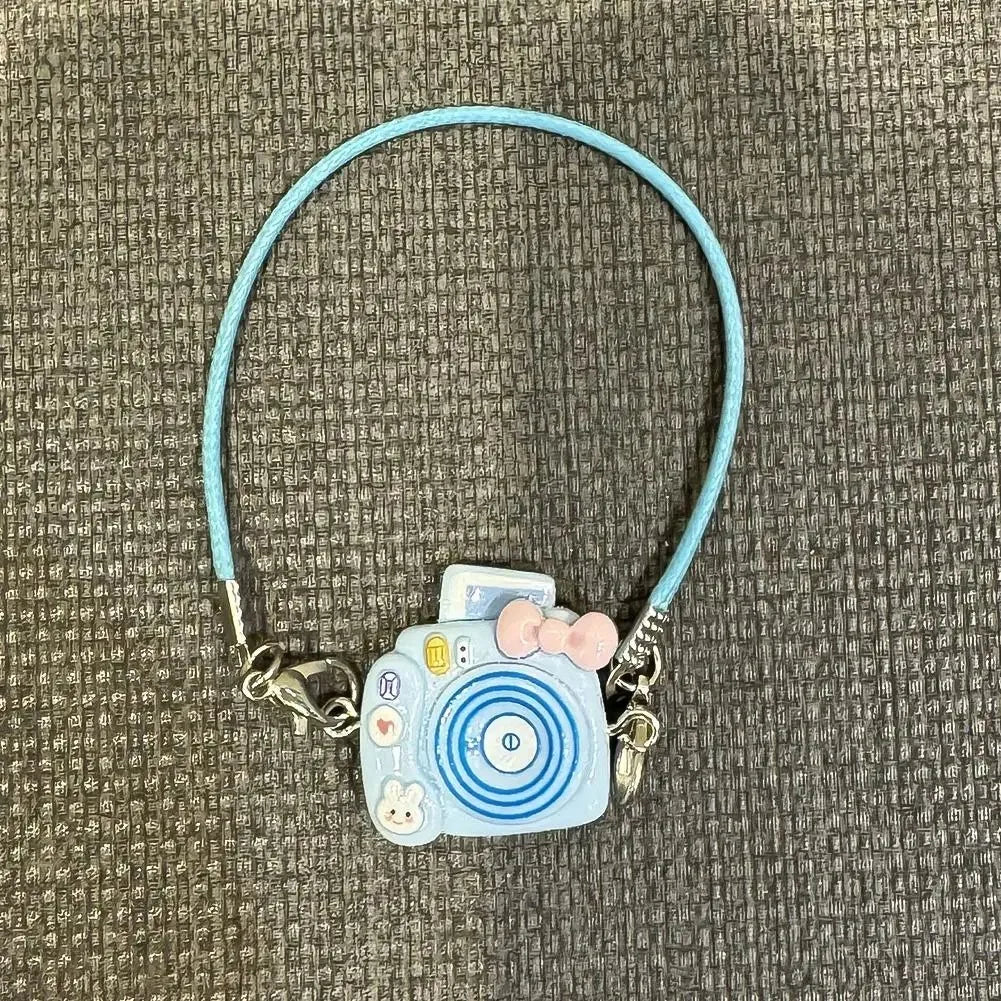 A light blue beaded necklace with a small camera charm and pink bow, suitable for a Labubu doll.