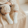 A pair of white fleece socks is shown resting on a beige knitted blanket.