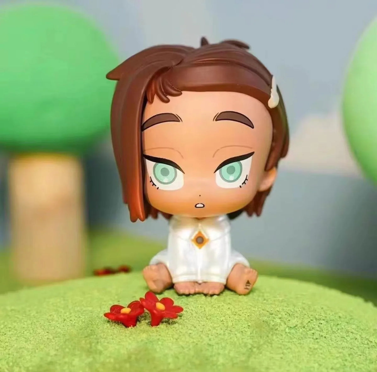 A mini figure collectible of a female character with brown hair and green eyes sitting on a bright green surface.