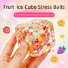 A hand holds a clear, colorful fruit ice cube stress ball with various fruit slices and candies inside.