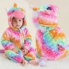 A plush rainbow unicorn hooded romper for a baby sitting on a white surface.