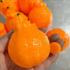 A hand holds a bright orange tangerine squishy stress relief toy with a green stem.