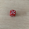 A single red acrylic die with five white pips is shown on a light wooden surface.