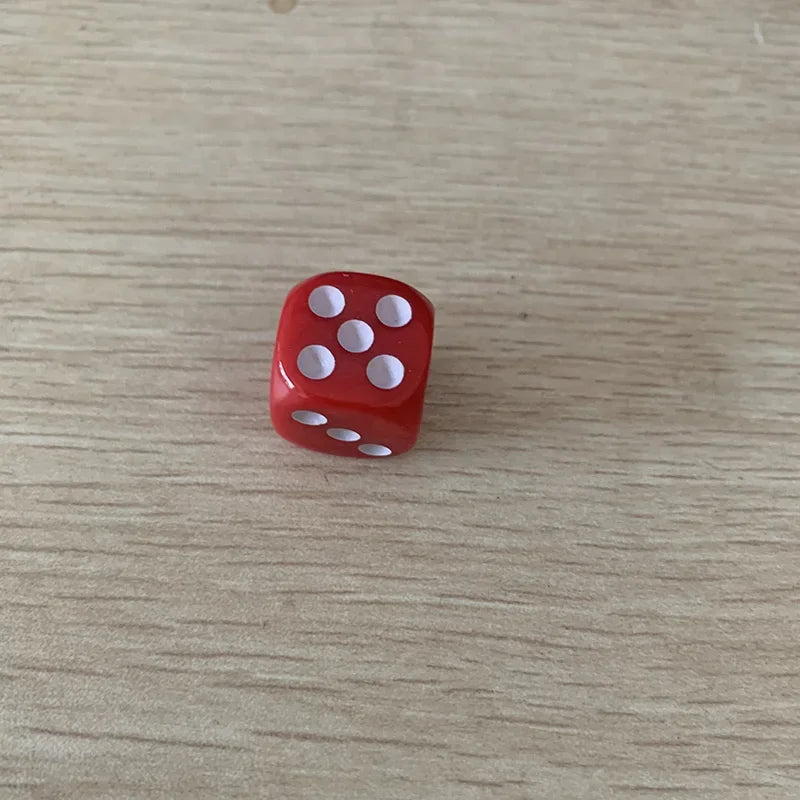 A single red acrylic die with five white pips is shown on a light wooden surface.