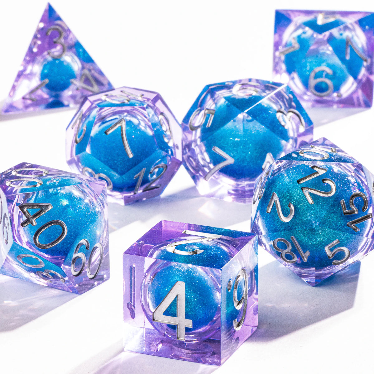 A collection of handmade liquid core polyhedral dice in various shades of blue and purple with a galaxy finish