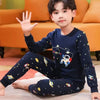 A young boy wearing a navy blue cotton pajama set with an astronaut print, sitting on the floor.