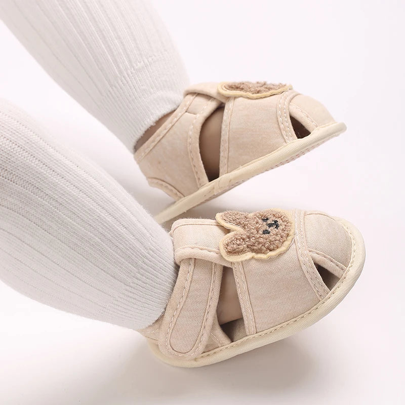 Pair of beige soft sole sandals for baby's first steps shown on a leg.