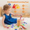 A young girl is playing with wooden toys including a coin, colored discs, and various wooden sticks on a white rug.