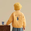 A child wearing a yellow padded jacket with a cat letter print, viewed from the back.