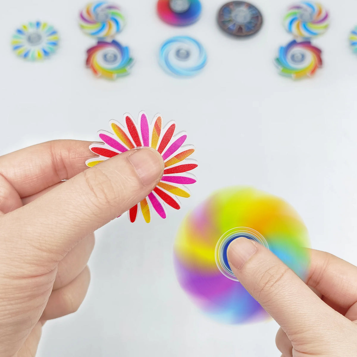 A hand holds a mini rainbow fidget spinner with colorful blades against a white background.