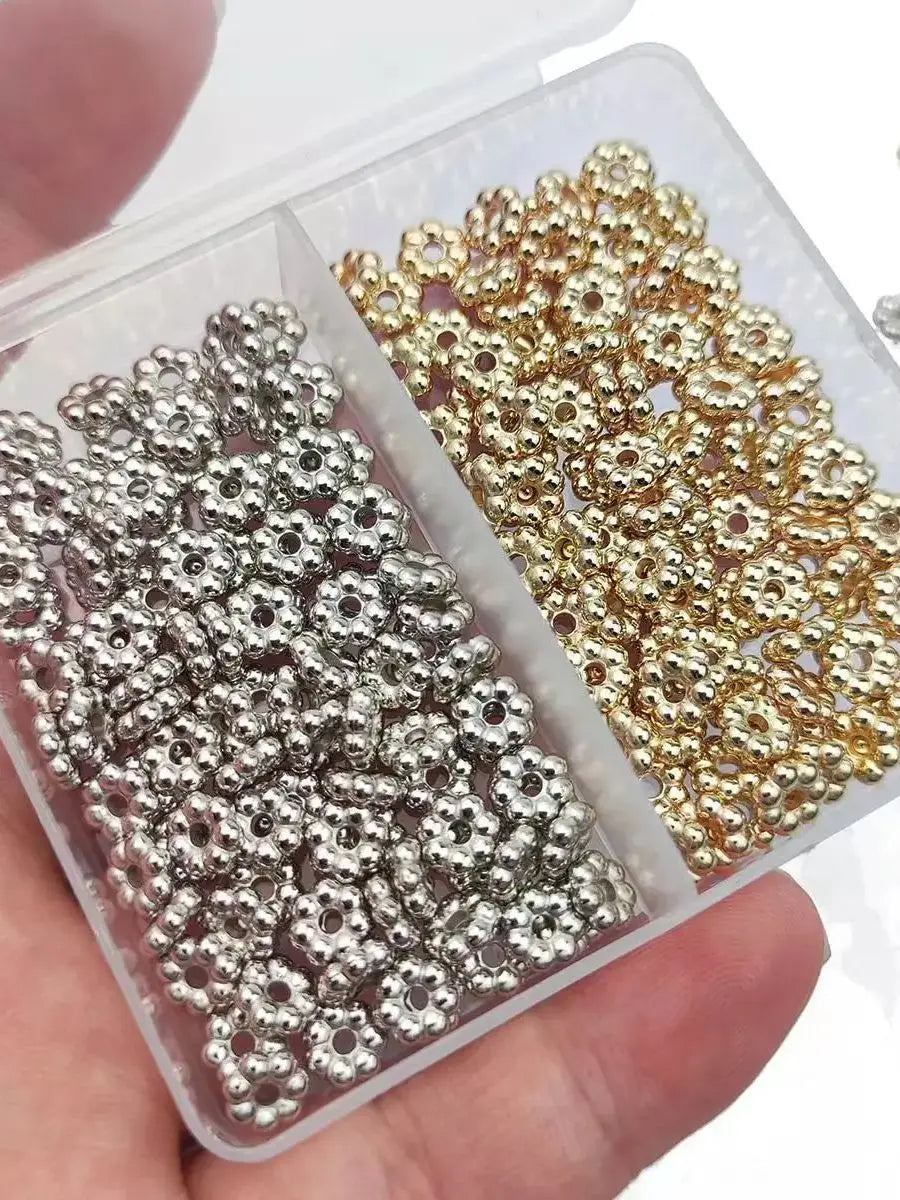 A clear plastic container holds two sets of small spacer beads: silver and gold-colored, for jewelry making.