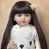 A lifelike 55 cm soft silicone baby doll with long dark hair wearing a cream-colored shirt and a flower accessory.