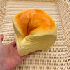 A yellow squishy toy shaped like a loaf of bread with an orange top, held in a hand on a woven mat.