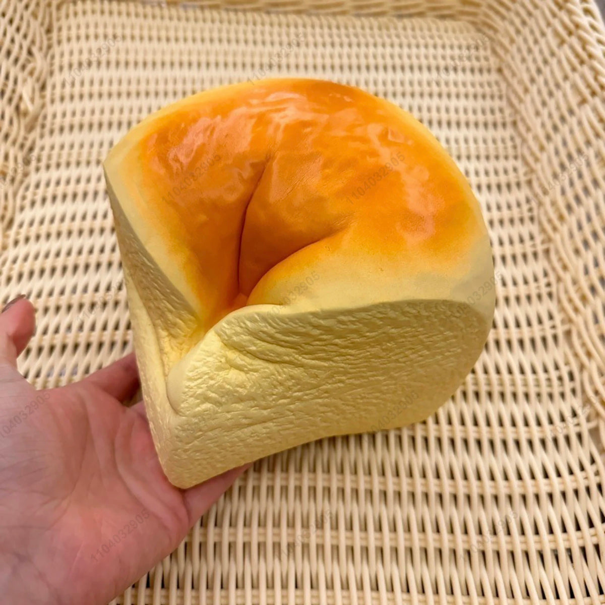 A yellow squishy toy shaped like a loaf of bread with an orange top, held in a hand on a woven mat.