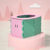 A pink and green foldable baby potty training seat is displayed on a round pedestal against a light pink background.