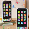 A digital phone screen displays various icons for music, stories, and learning activities, with a physical toy phone nearby.