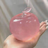 A hand holds a translucent pink squishy stress relief toy shaped like an apple with a clear top.