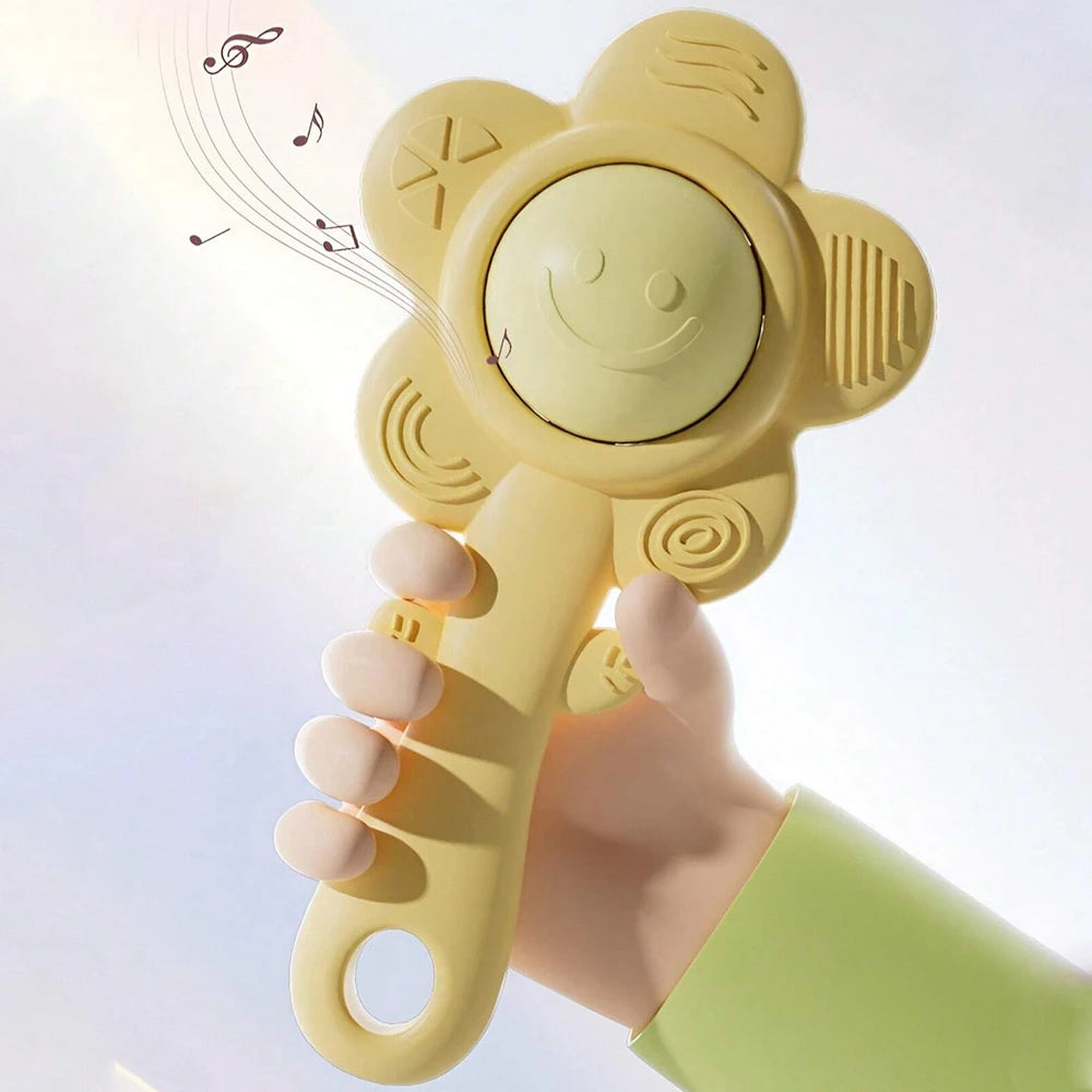 A hand holds a yellow sensory teething rattle with a smiley face and musical notes floating nearby.