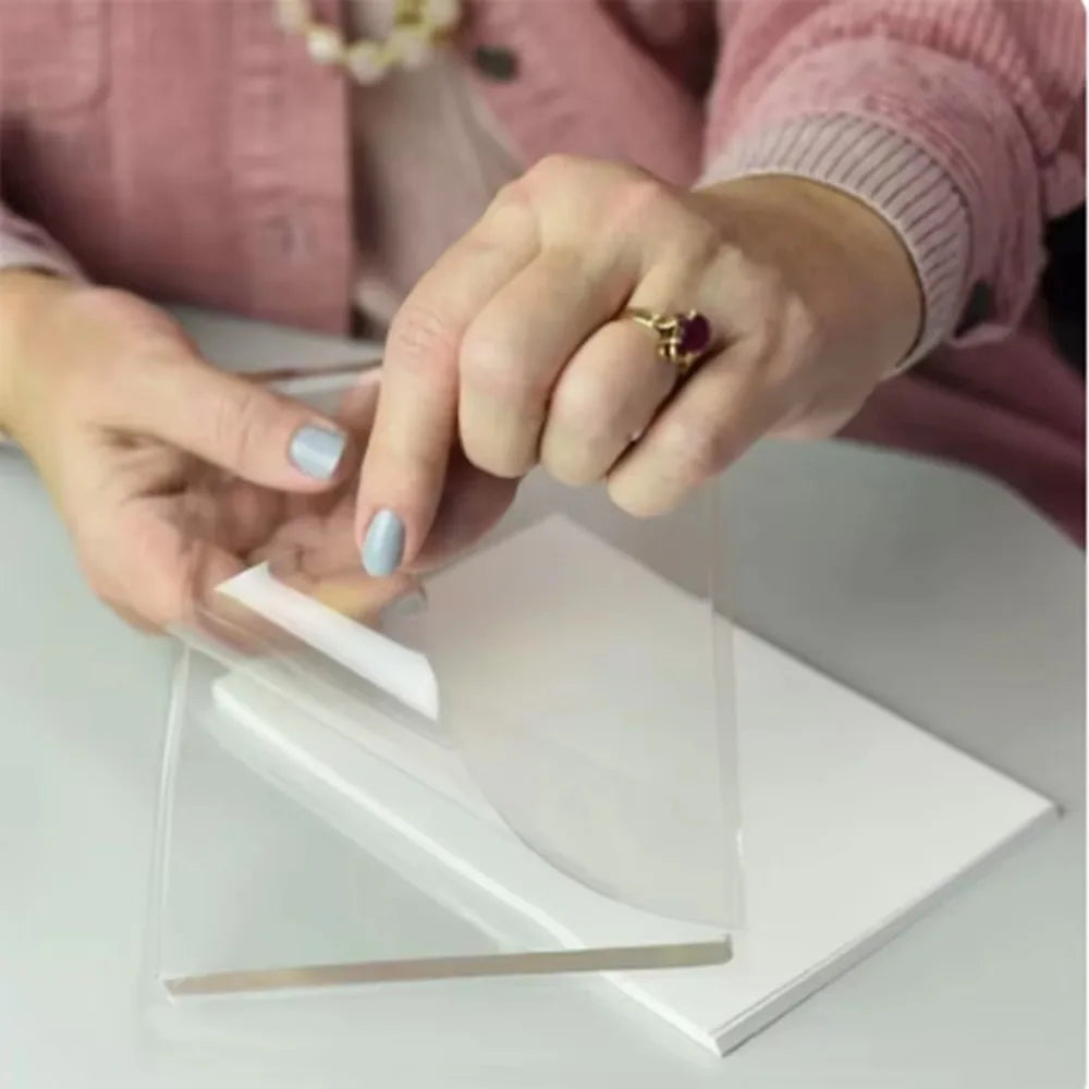 A person is using a clear silicone printing plate to apply ink onto paper for mixed media art.
