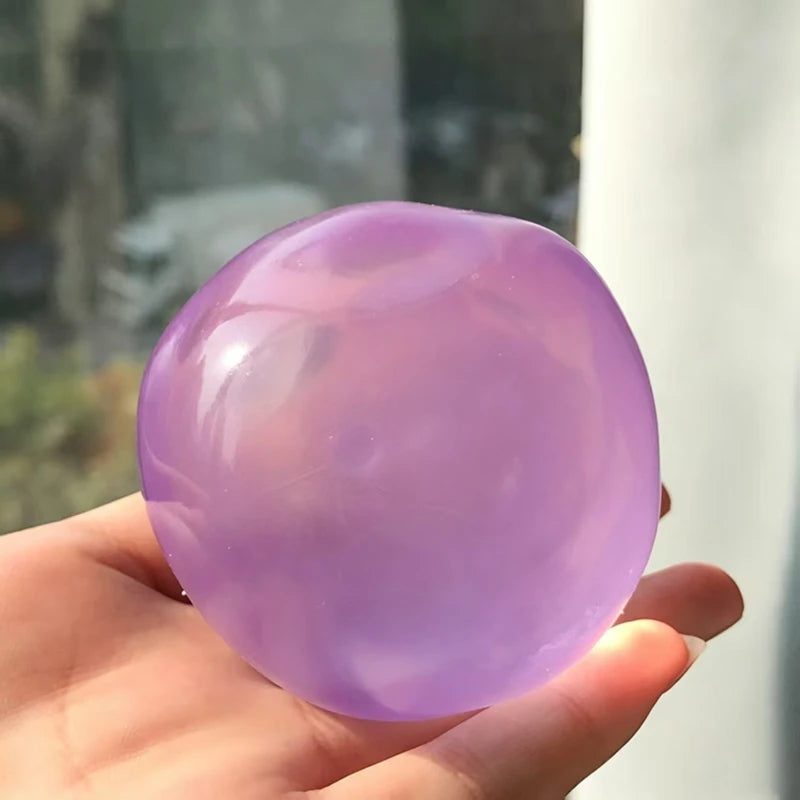 A hand holds a smooth, translucent purple coconut oil squishy stress ball.