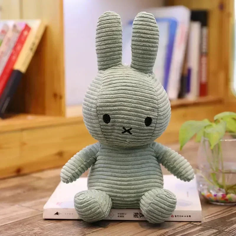 A soft, light green Miffy plush toy rabbit sitting on a book.