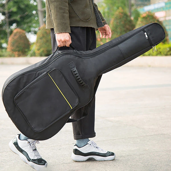 A person is holding a black acoustic guitar bag with yellow accents outdoors.