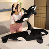 A young woman is holding a black and white orca whale plush toy in a studio setting.