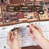 Hands assemble a wooden miniature house kit puzzle featuring an illuminated owl post office and furniture.