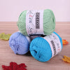 Three skeins of pure cotton knitting yarn in green, blue, and cyan colors are displayed on a wooden surface.