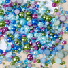 A colorful mix of iridescent resin and rhinestone pearls in shades of blue, green, purple, and pink scattered on a light surf