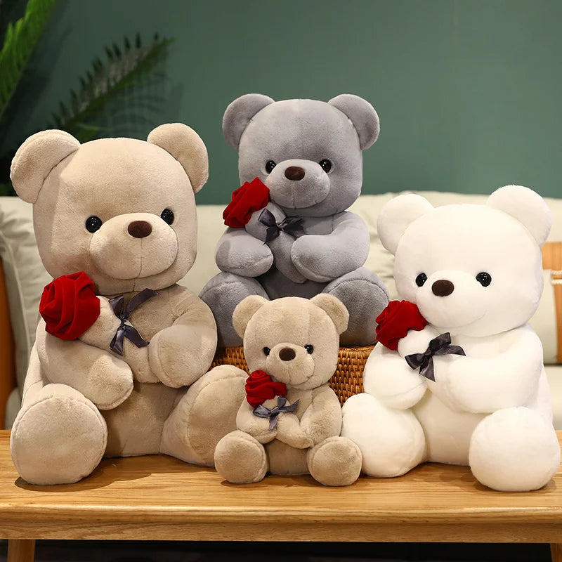 A collection of three plush teddy bears in various shades of gray and white, some holding red roses.