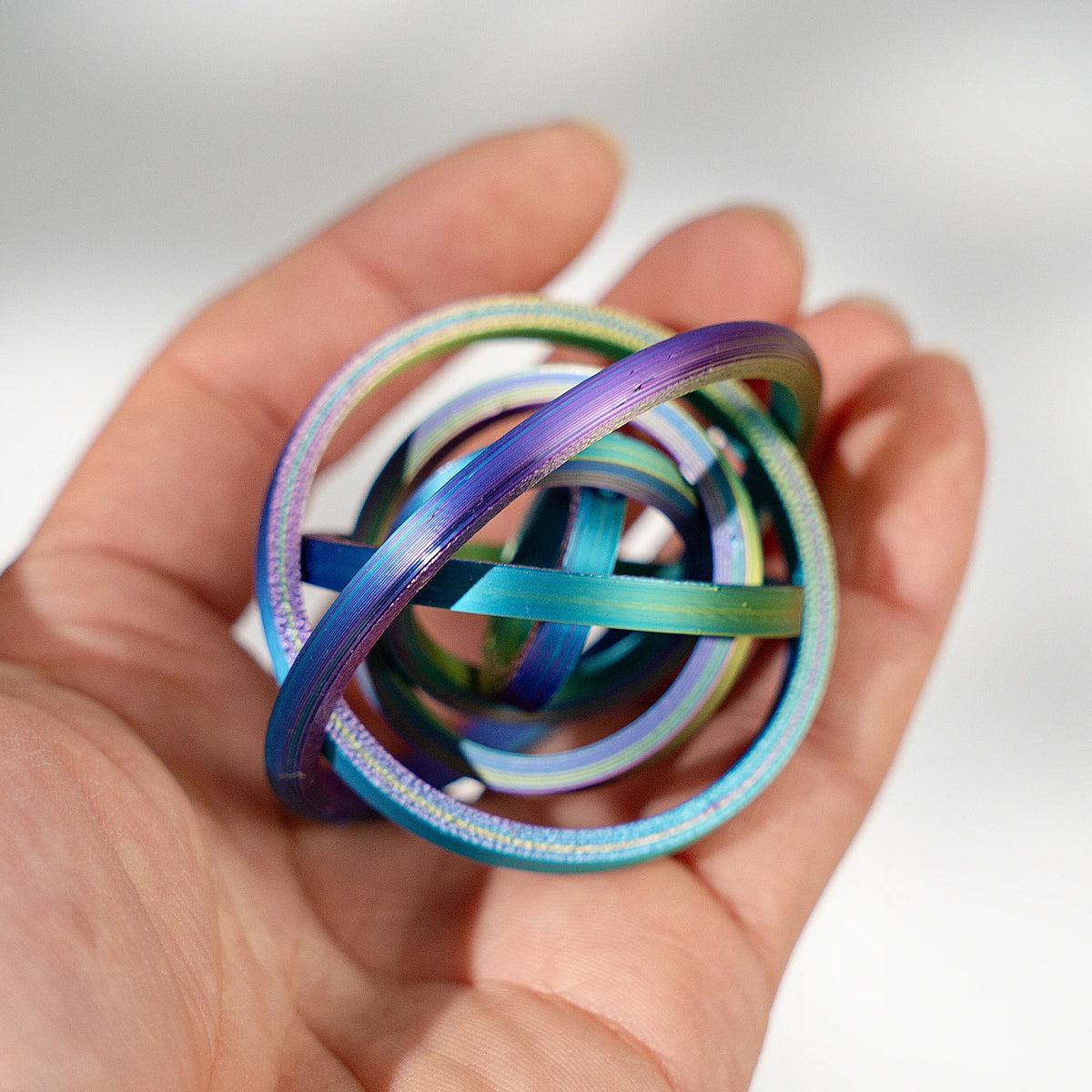 A hand holds a stack of colorful, iridescent spinner rings with various shades of blue and green.