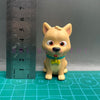 A playful cartoon PVC figurine of a dog with orange fur and large eyes, standing next to a ruler.