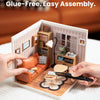 Hands assemble a wooden miniature house kit for a cozy living lounge with an LED light.