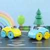 A yellow and blue clockwork duck bath toy car is positioned on a gray track with green fence and a green tree in the backgrou
