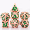 A set of seven metal dice in rose gold and green enamel, including a pyramid die and various polyhedral dice.