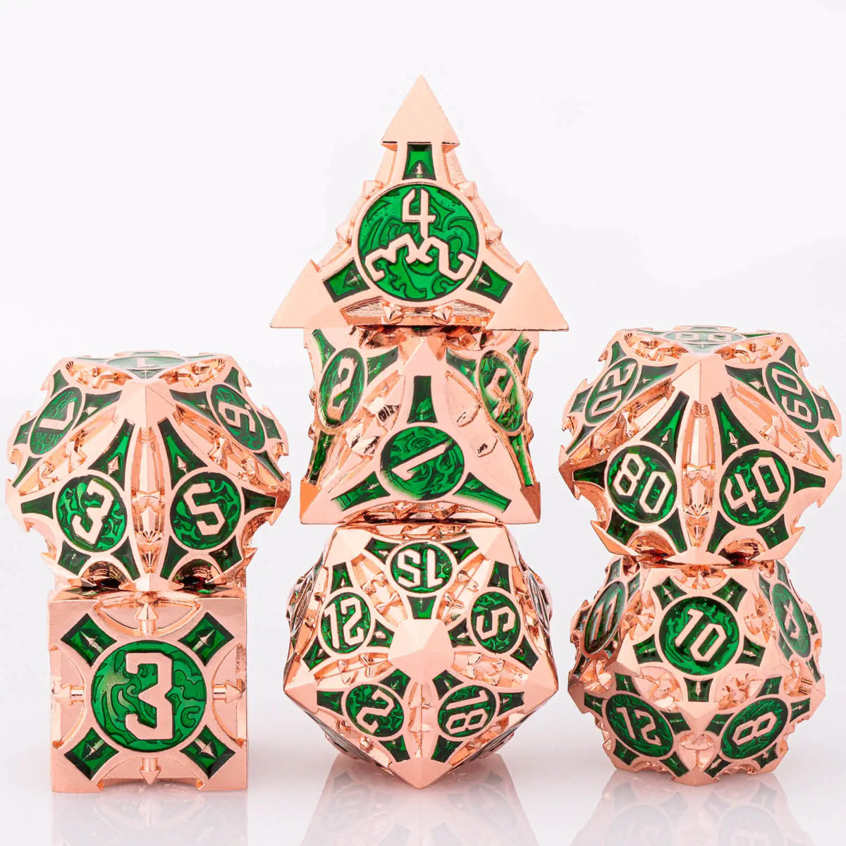 A set of seven metal dice in rose gold and green enamel, including a pyramid die and various polyhedral dice.