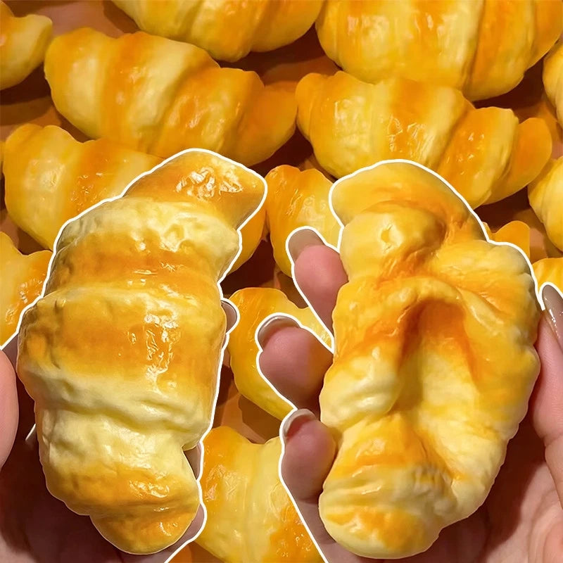 A hand holds a golden croissant pastry baked in a pan, showing its flaky texture.