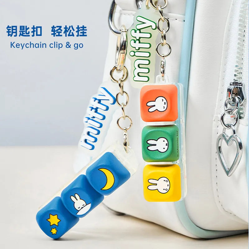 A collection of Miffy anime keycap pendants in various colors attached to a keychain clip on a white bag.
