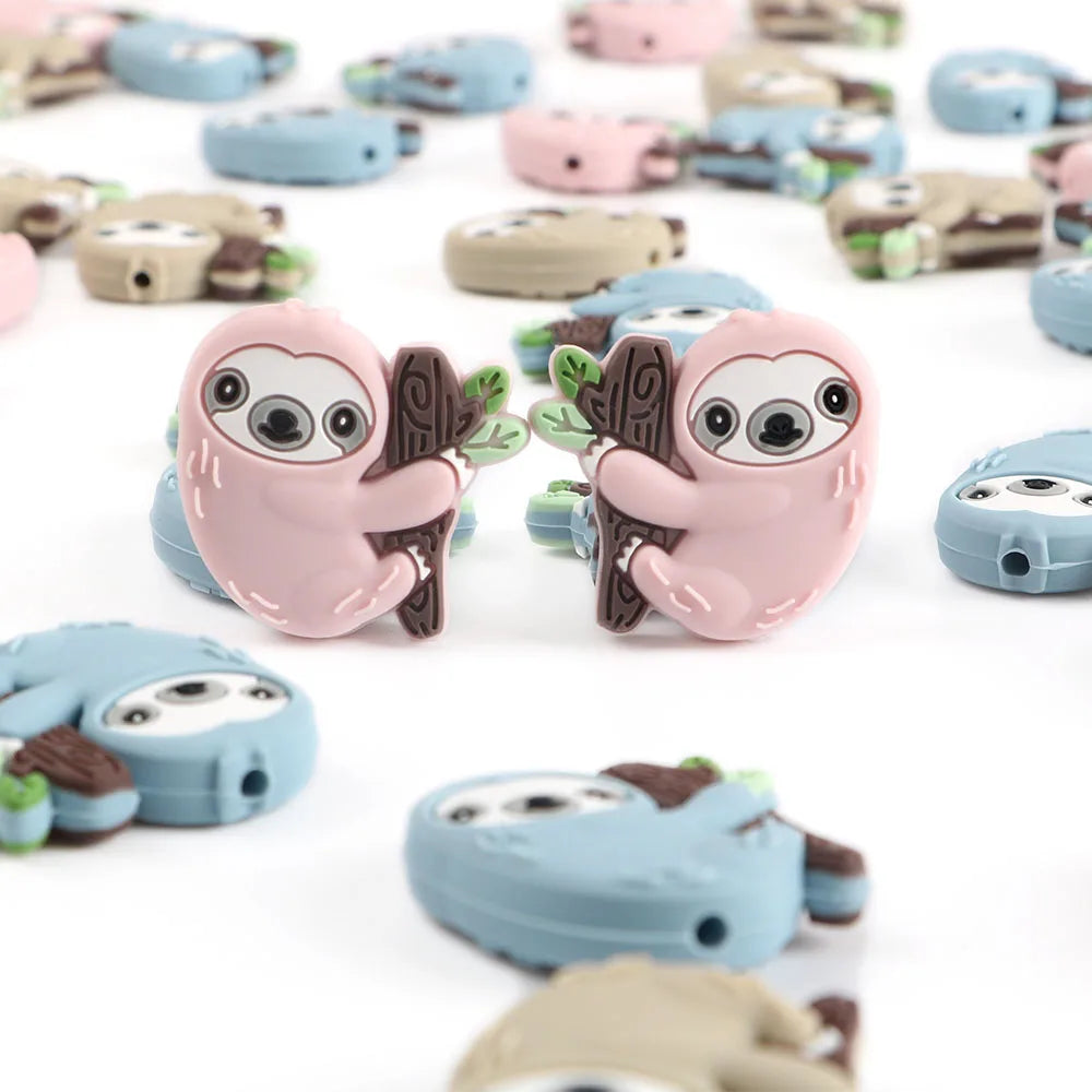 A collection of adorable sloth silicone beads in various shades of pink, blue, and beige for DIY crafts.
