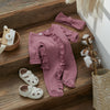 A pink knit ruffle romper for a baby girl with a matching pink bow and headband displayed on a wooden surface.