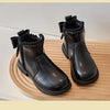 A pair of black girls' ankle boots with a bow-knot detail and side zipper resting on a wooden surface.