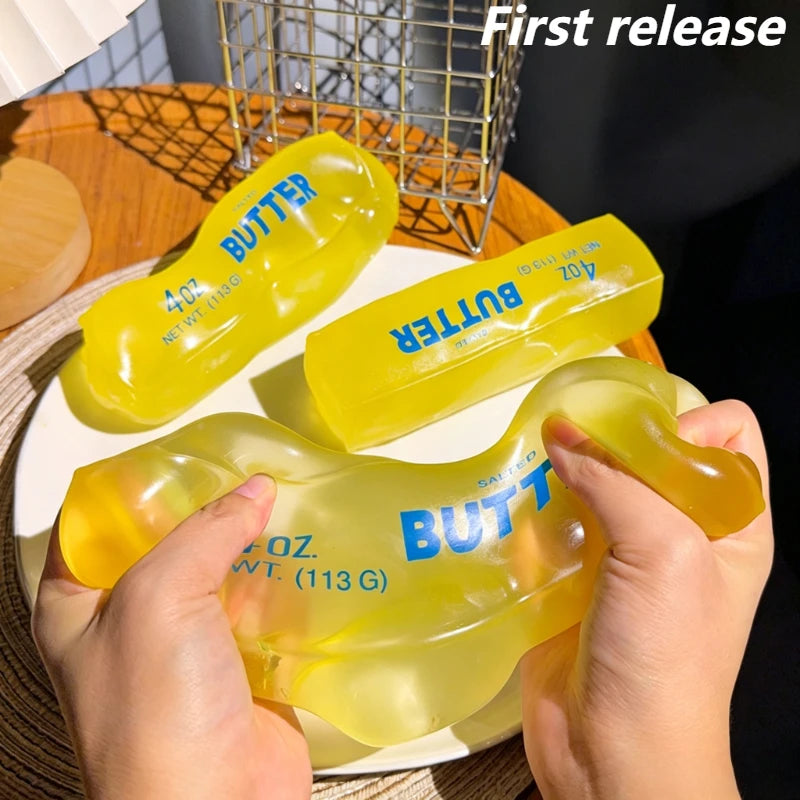 A hand holds a yellow butter squishy stress relief toy next to a metal grid and a plate.