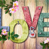 Wooden letters spelling LOVE decorated with pink flowers and green leaves